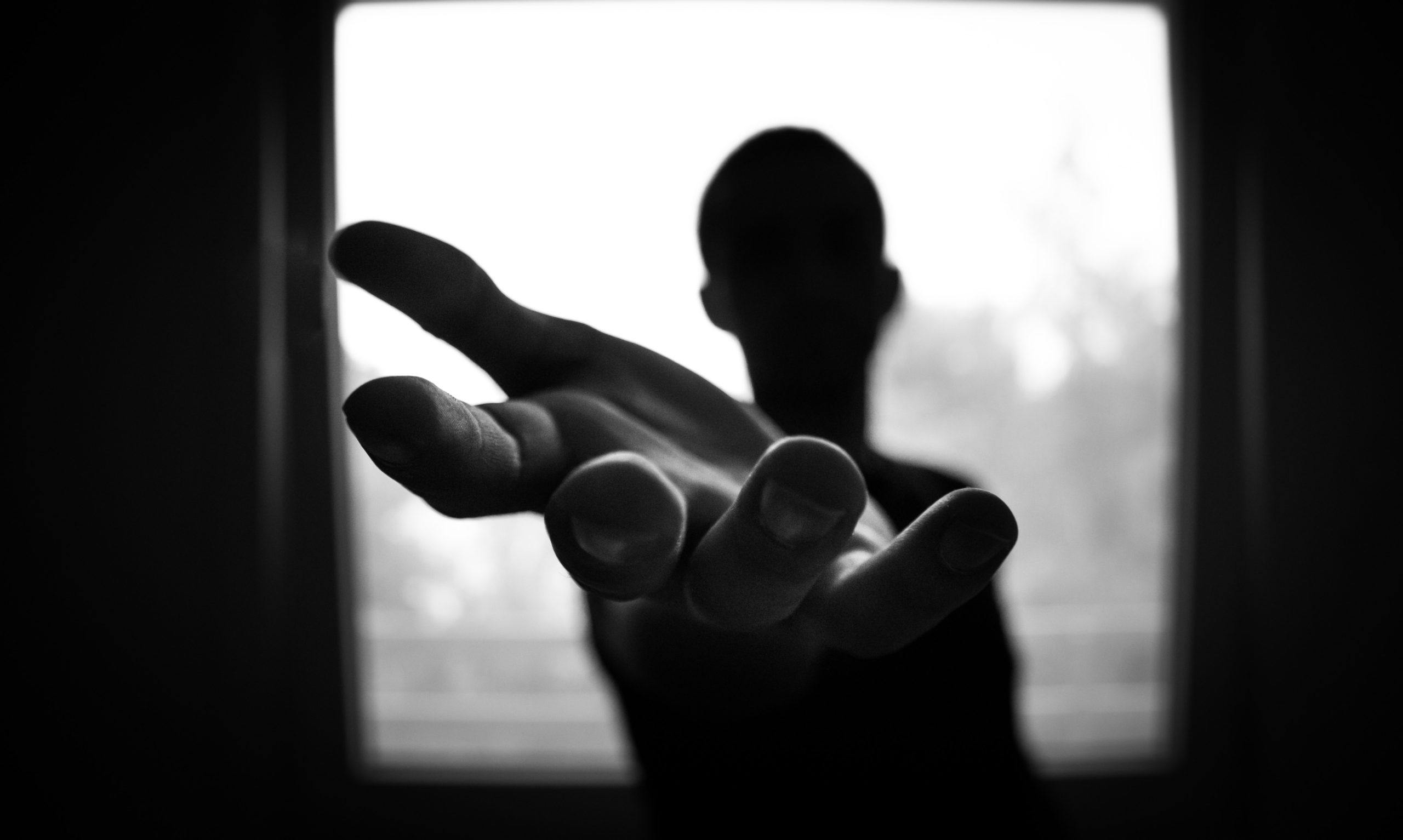 Silhueta de estende a mão em frente uma janela.